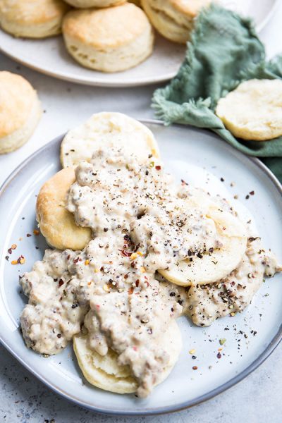 Sausage gravy is smothering the halved biscuits and is topped with lots of cracked pepper.