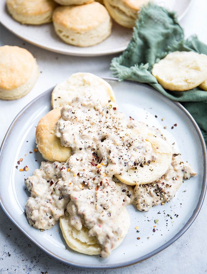 Sausage gravy is smothering the halved biscuits and is topped with lots of cracked pepper.