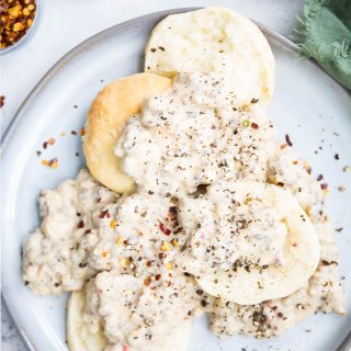 Sausage gravy is smothering the halved biscuits and is topped with cracked pepper and red pepper flakes.