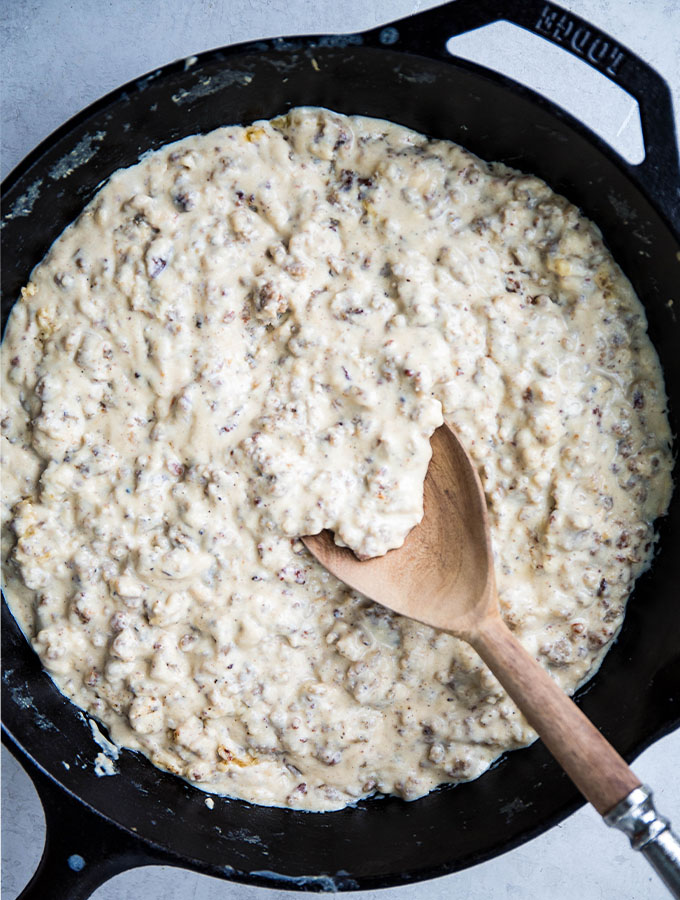 Sausage gravy is made in a cast iron pan with 4 simple ingredients and stirred with a spoon.