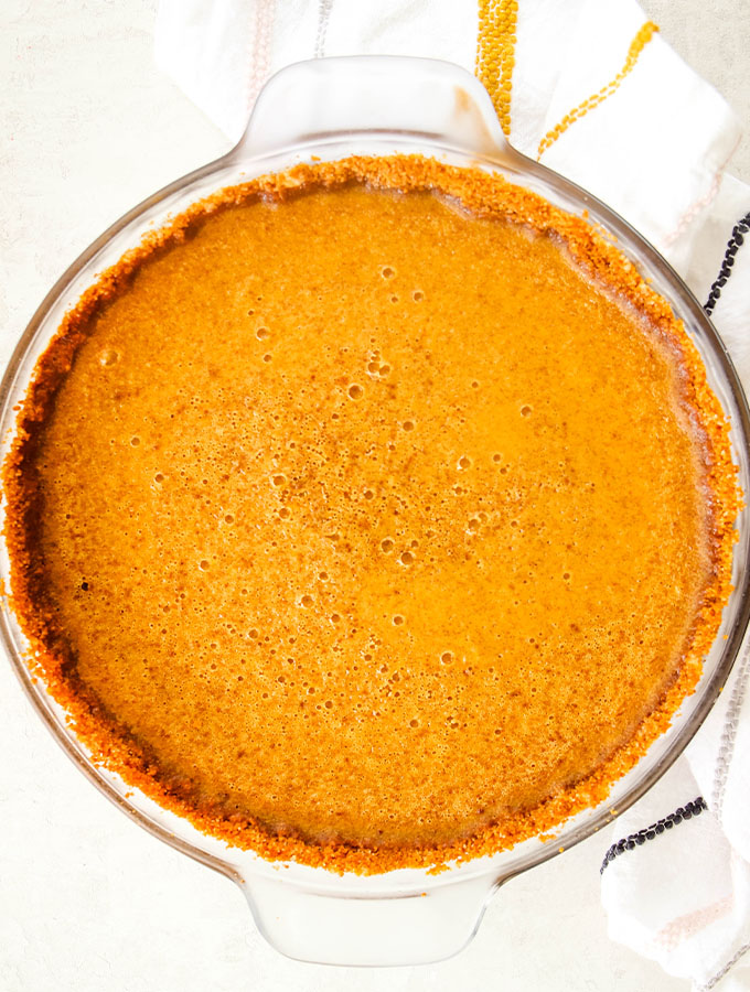Pumpkin pie from scratch is baked in a glass pie dish and cooled at room temperature.