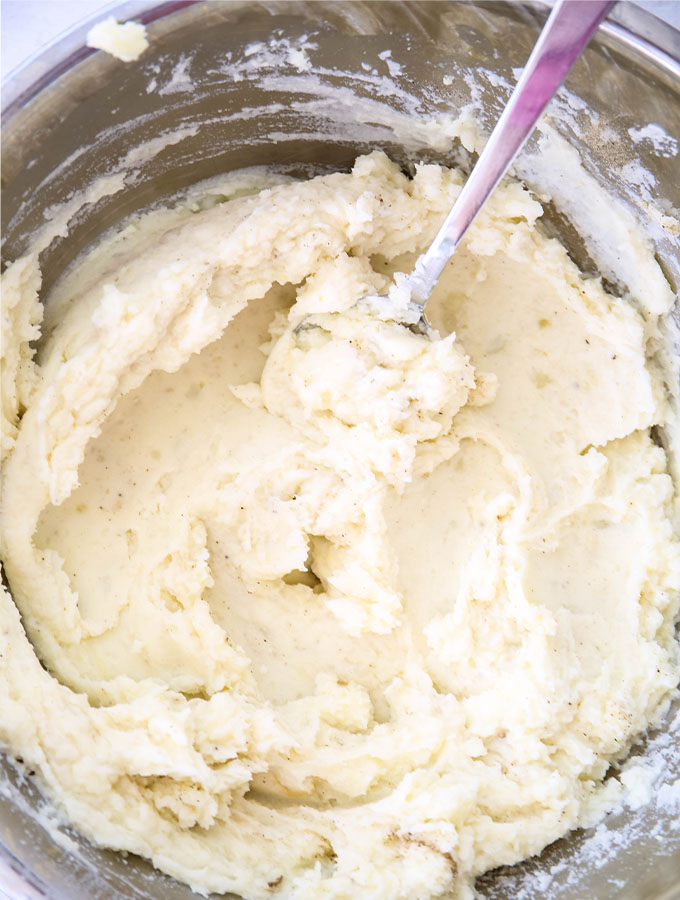 The potatoes are mashed in a large bowl until the texture is smooth.