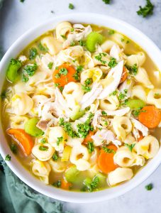Chicken tortellini soup is plated in a white bowl and topped with fresh parsley for extra flavor.