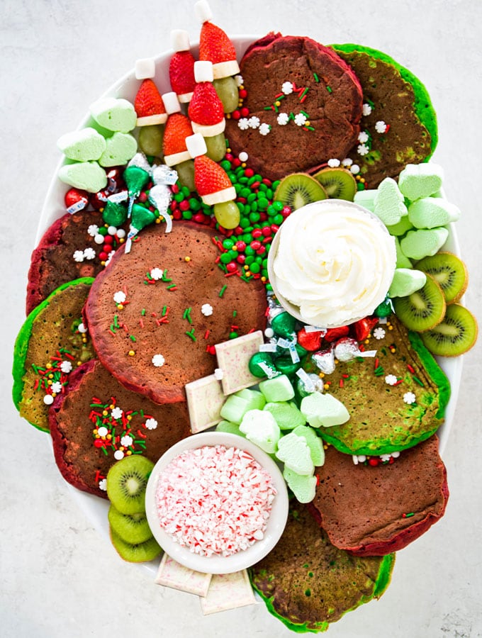 A Christmas breakfast board is filled with pancakes, fruits, candies, and homemade whipped cream.