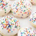 Italian anise cookies are plated on a white plate and topped with nonparelli sprinkles.