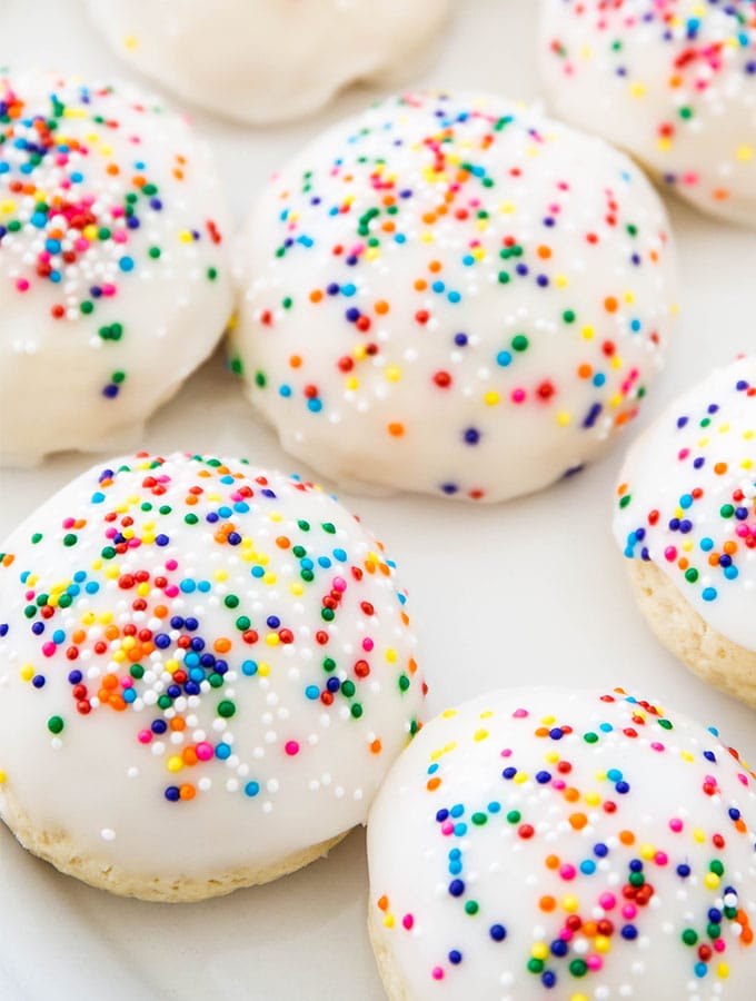 Italian anise cookies are plated on a white plate and topped with nonparelli sprinkles.
