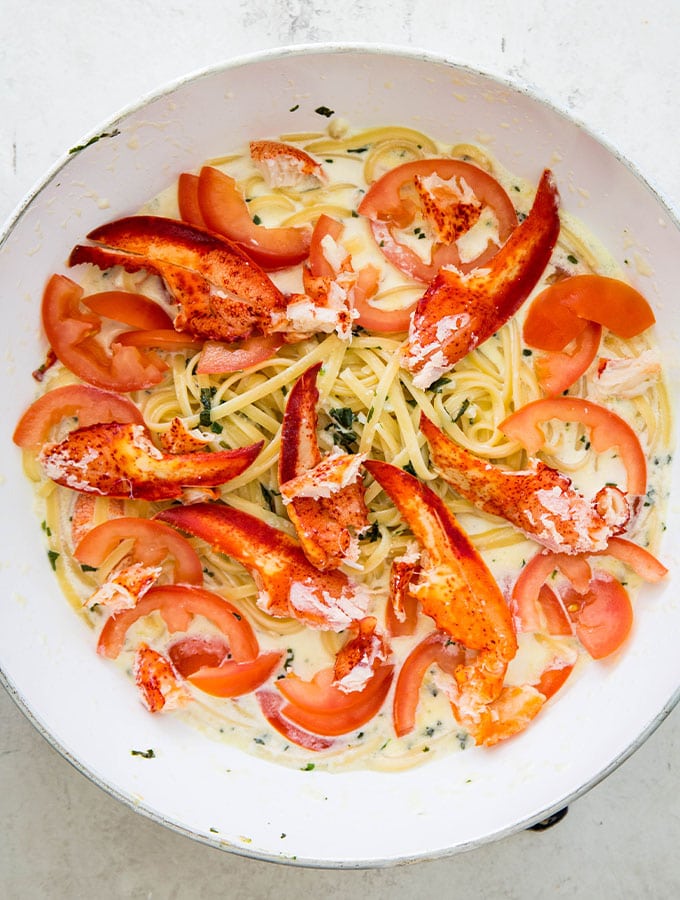 The cream sauce, pasta, lobster meat, and the tomatoes are tossed in a large pan to finish the dish.