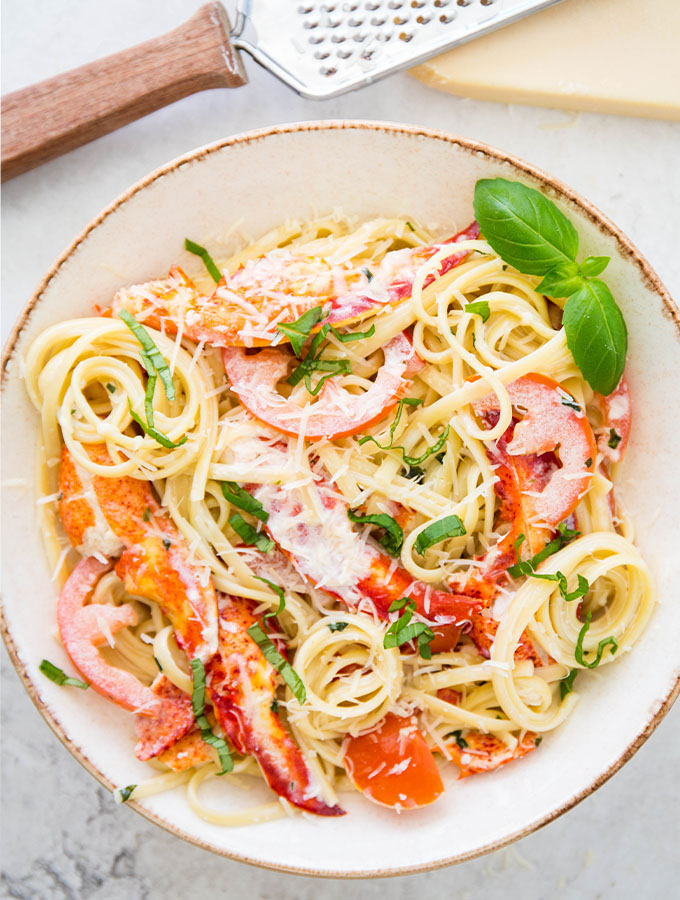 Lobster pasta is plated in a white bowl and topped with freshly grated parmesan cheese.