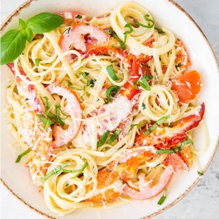 Lobster pasta is plated in a white bowl and topped with parmesan cheese and fresh basil.