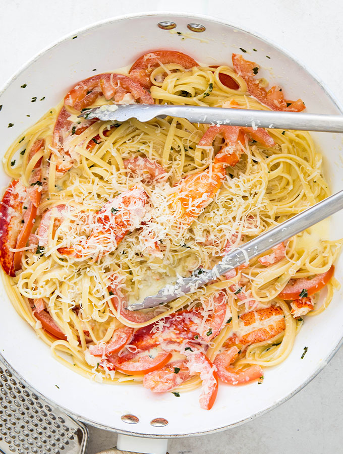 Lobster pasta is tossed with tongs in a large pan to finish the dish.
