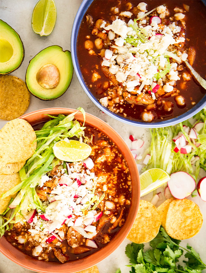 Turkey pozole is plated in two bowls and topped with chips, radishes, and cheese.