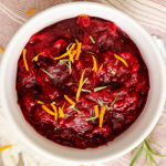 Cranberry sauce is plated in a white bowl and topped with orange zest.