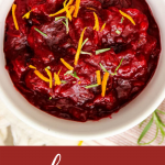 Cranberry sauce is plated in a white bowl and topped with rosemary and orange peel.