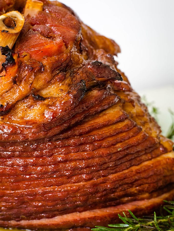 A spiral ham is glazed and placed on a serving platted with fresh herbs for serving.