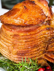A fully cooked spiral ham is baked then plated with fresh herbs as garnishes.