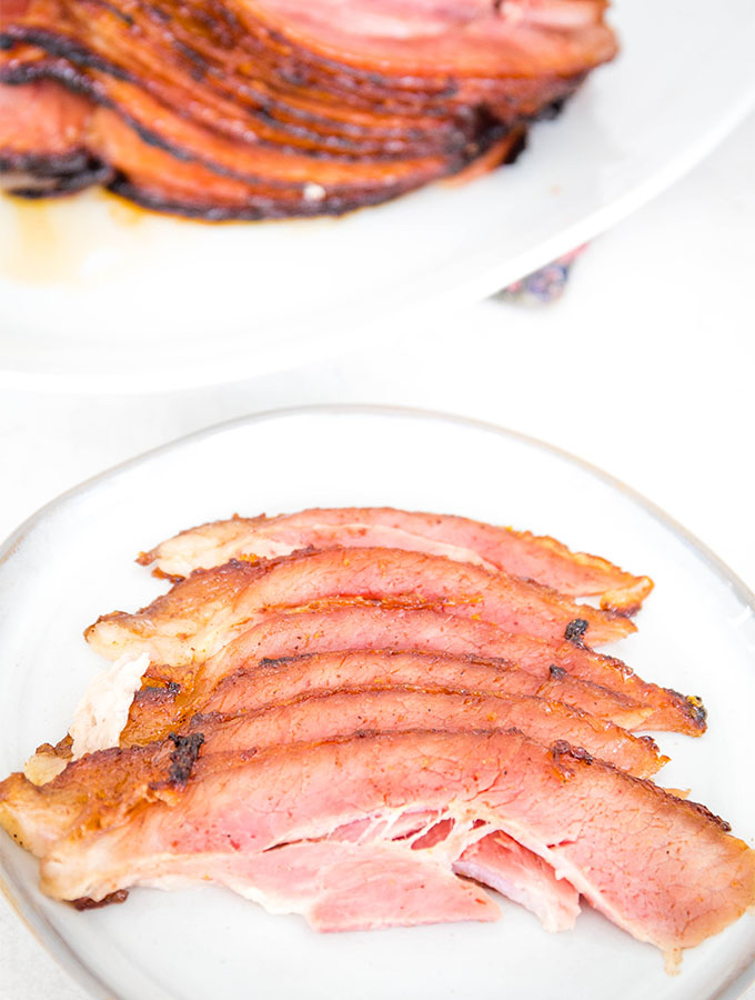 Ham is sliced and plated on a gray plate next to the ham.