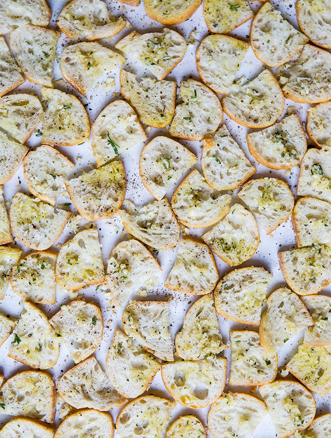 Sliced bread is coated in olive oil, garlic, parmesan, and herbs before it is baked to make croutons.