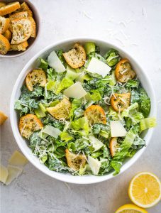 Homemade Caesar salad is plated in a white bowl and topped with cheese and croutons.