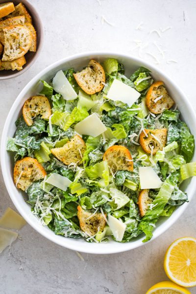 Homemade Caesar salad is plated in a white bowl and topped with cheese and croutons.