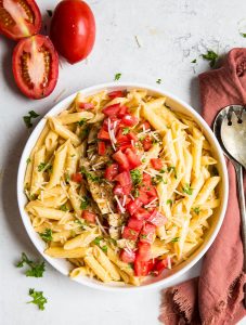Cajun Chicken Pasta is plated in a white bowl and placed next to tomatoes, a napkin, and forks.