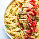 Creamy cajun chicken pasta is plated in a white bowl and topped with tomatoes and cheese.