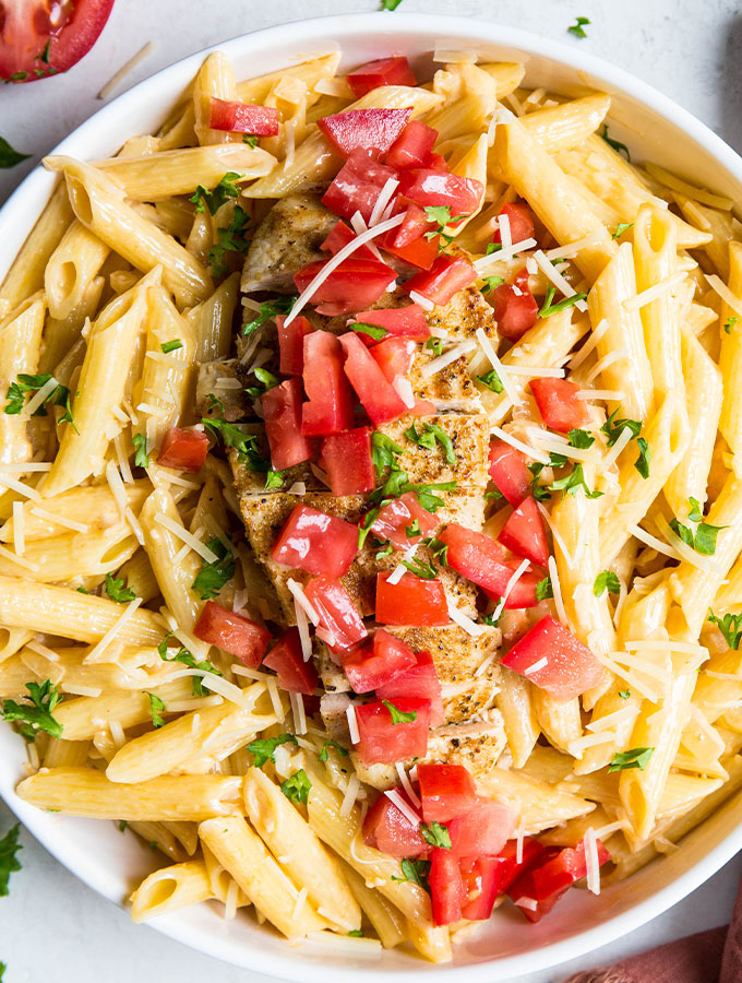 Creamy cajun chicken pasta is plated in a white bowl, topped with tomatoes, cheese, and parsley.
