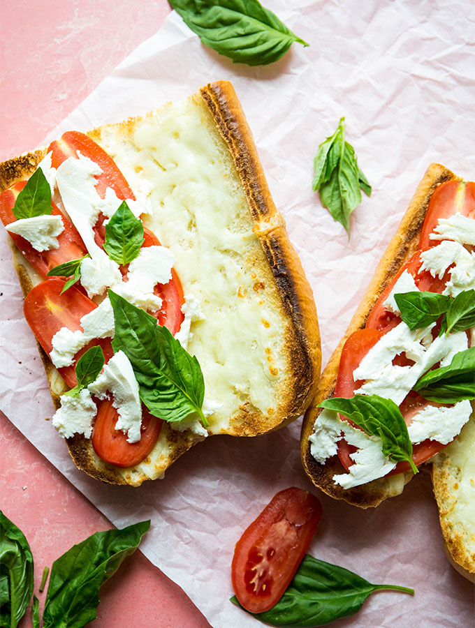 Basil and tomato sliced are stacked on the bread before the chicken is placed on it.