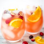 Two wine glasses are full of ice and sangria and topped with oranges and cranberries.