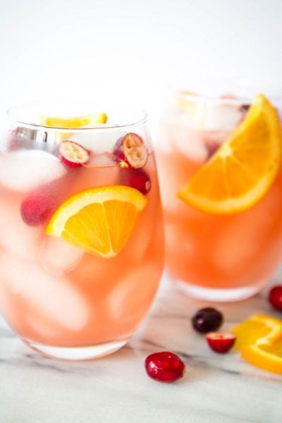 Two wine glasses are full of ice and sangria and topped with oranges and cranberries.