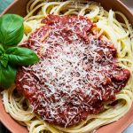 Red wine pasta sauce is placed on top of the spaghetti pasta and is plated in a red bowl.