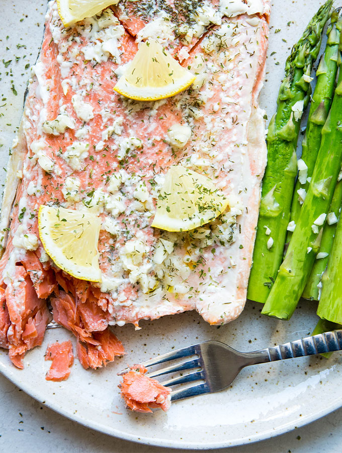 Salmon is plated next to asparagus on a brown speckled plate with a fork.a
