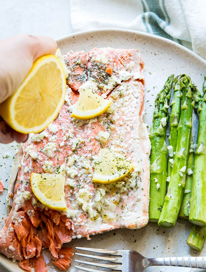 A hand is squeezing a lemon over the salmon and asparagus on a brown plate.