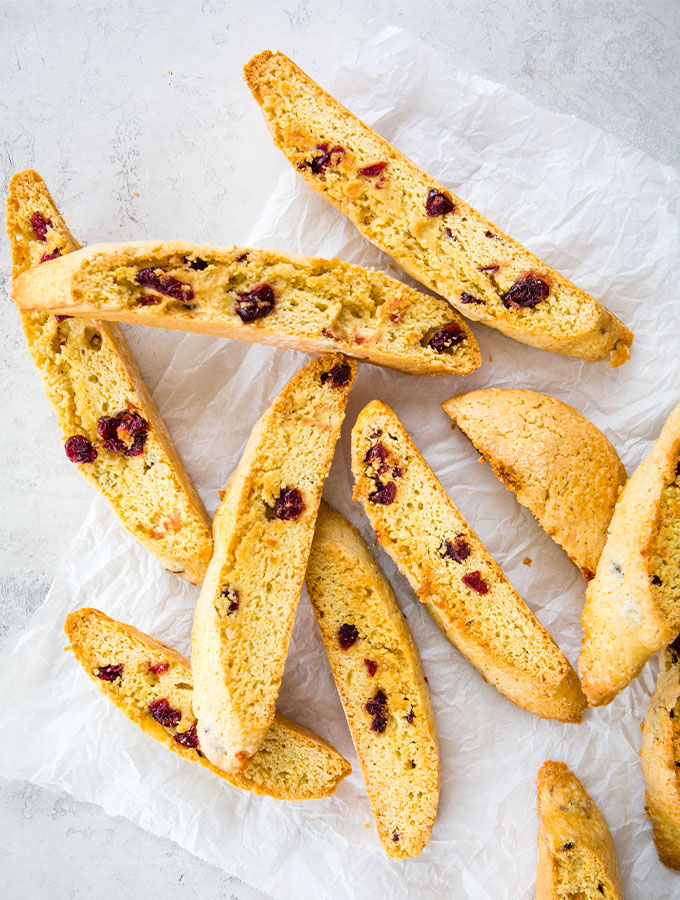 Cranberry orange biscotti cookies are cut, baked, and displayed on a piece of parchment paper.
