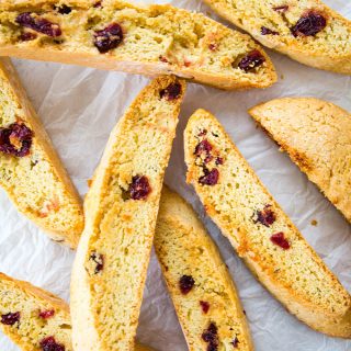 Cranberry orange biscotti cookies are stacked on white parchment paper.