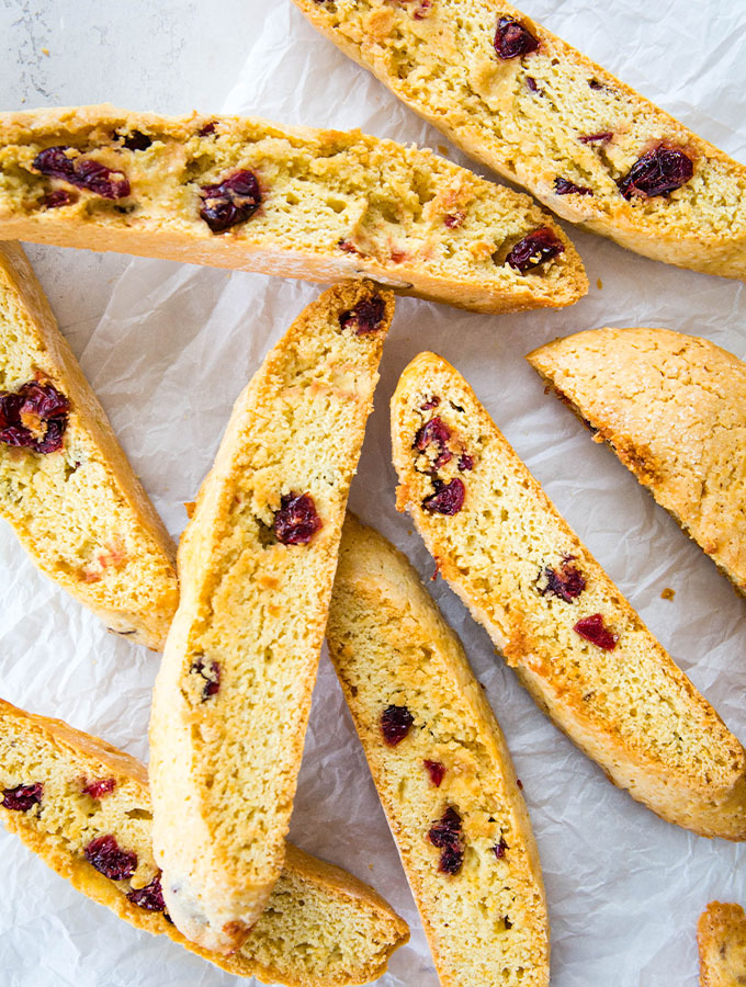 Cranberry orange biscotti cookies are stacked on white parchment paper.