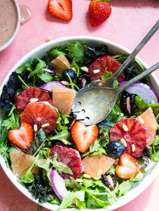 The winter salad is plated in a white bowl next to a bowl of salad dressing and strawberries.