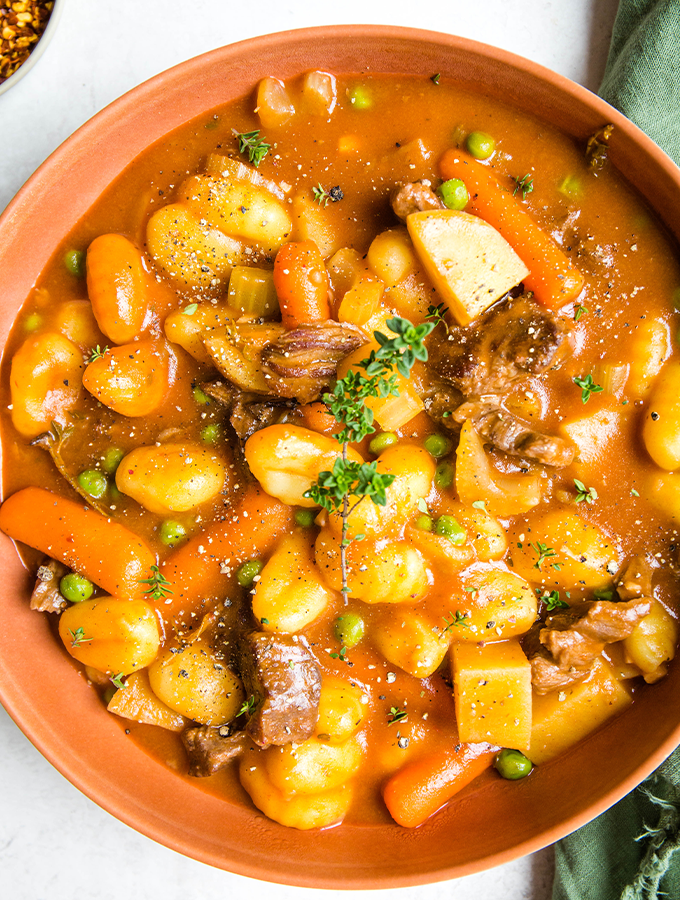 Gnocchi beef stew is topped with freshly cracked pepper and a sprig of thyme.