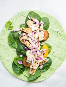 Italian chicken wrap is topped with chicken, spinach, red onion, and tomato.