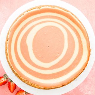 Strawberries and Cream Cheesecake is plated on a cake stand next to sliced strawberries.