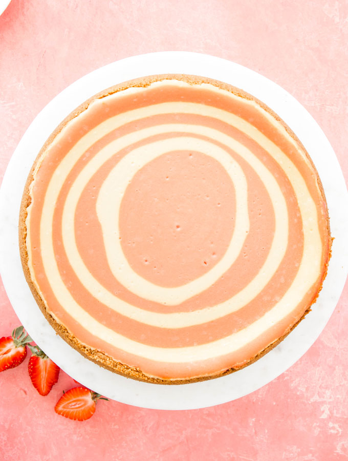 Strawberries and Cream Cheesecake is plated on a cake stand next to sliced strawberries.