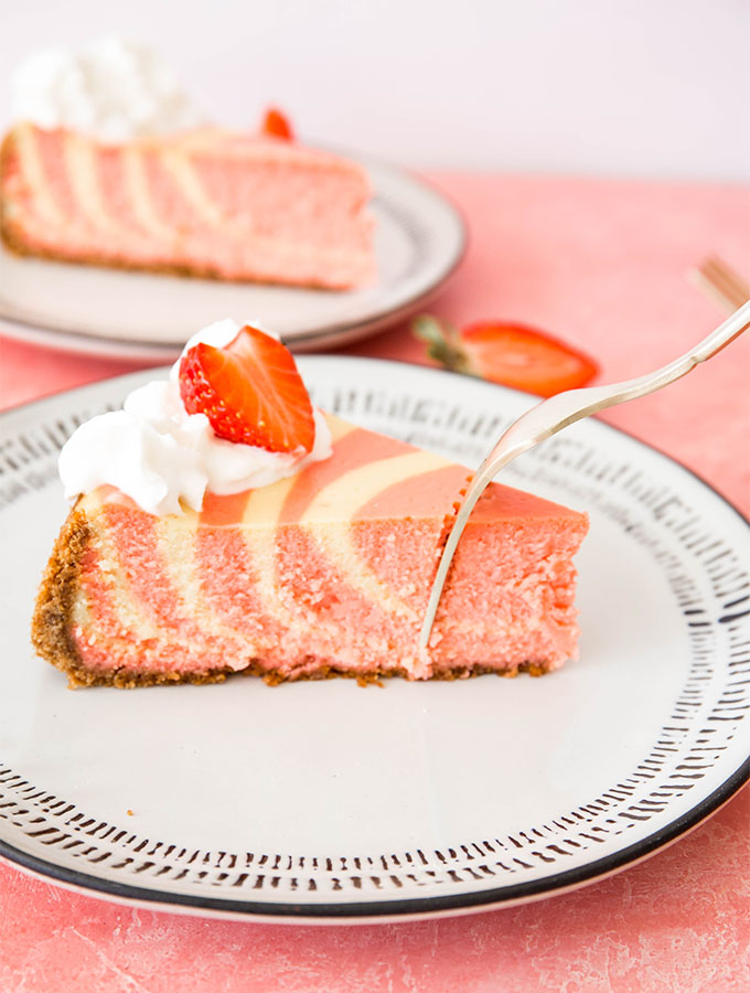 A fork is piercing the cheesecake slice that is plated on a white plate.