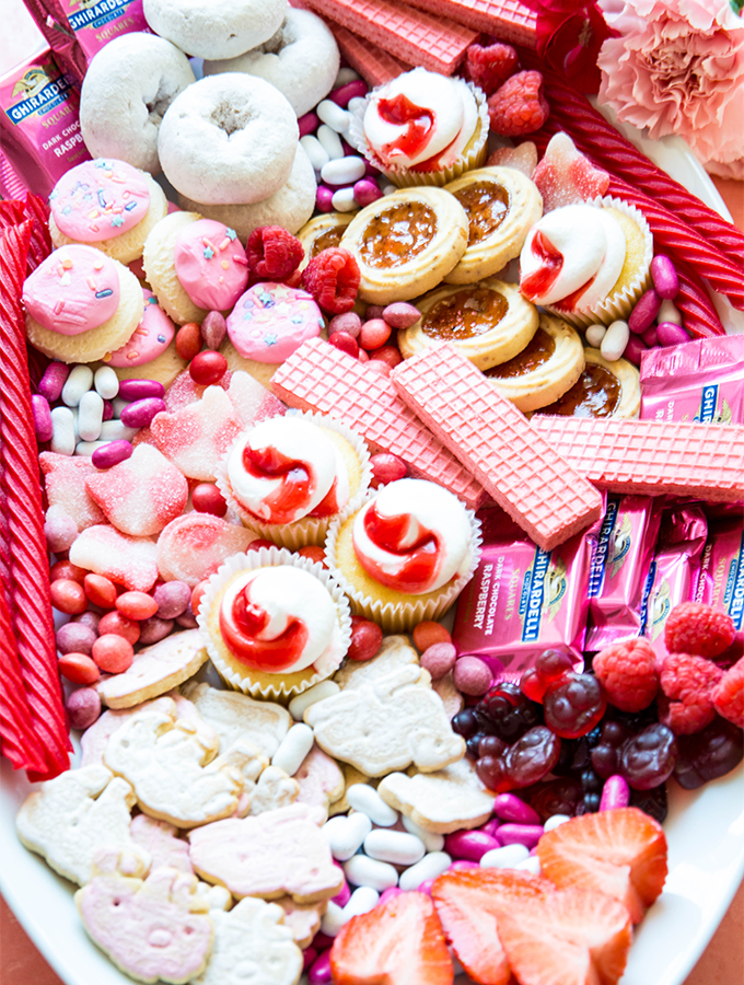Frosted animal crackers, chocolates, wafers, donuts, and candies are placed around the charcuterie board.