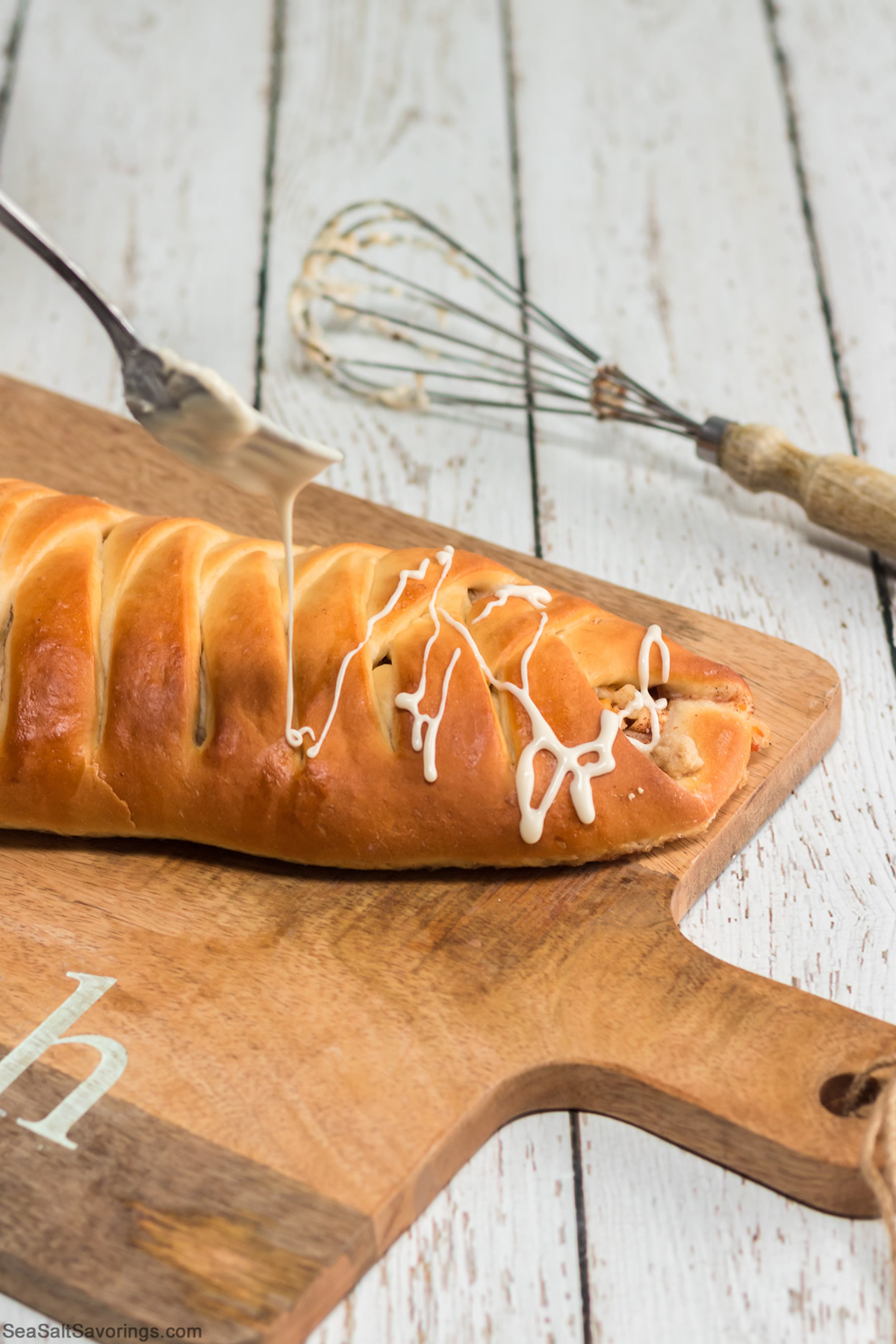 fresh baked log of apple bread getting icing drizzled on top