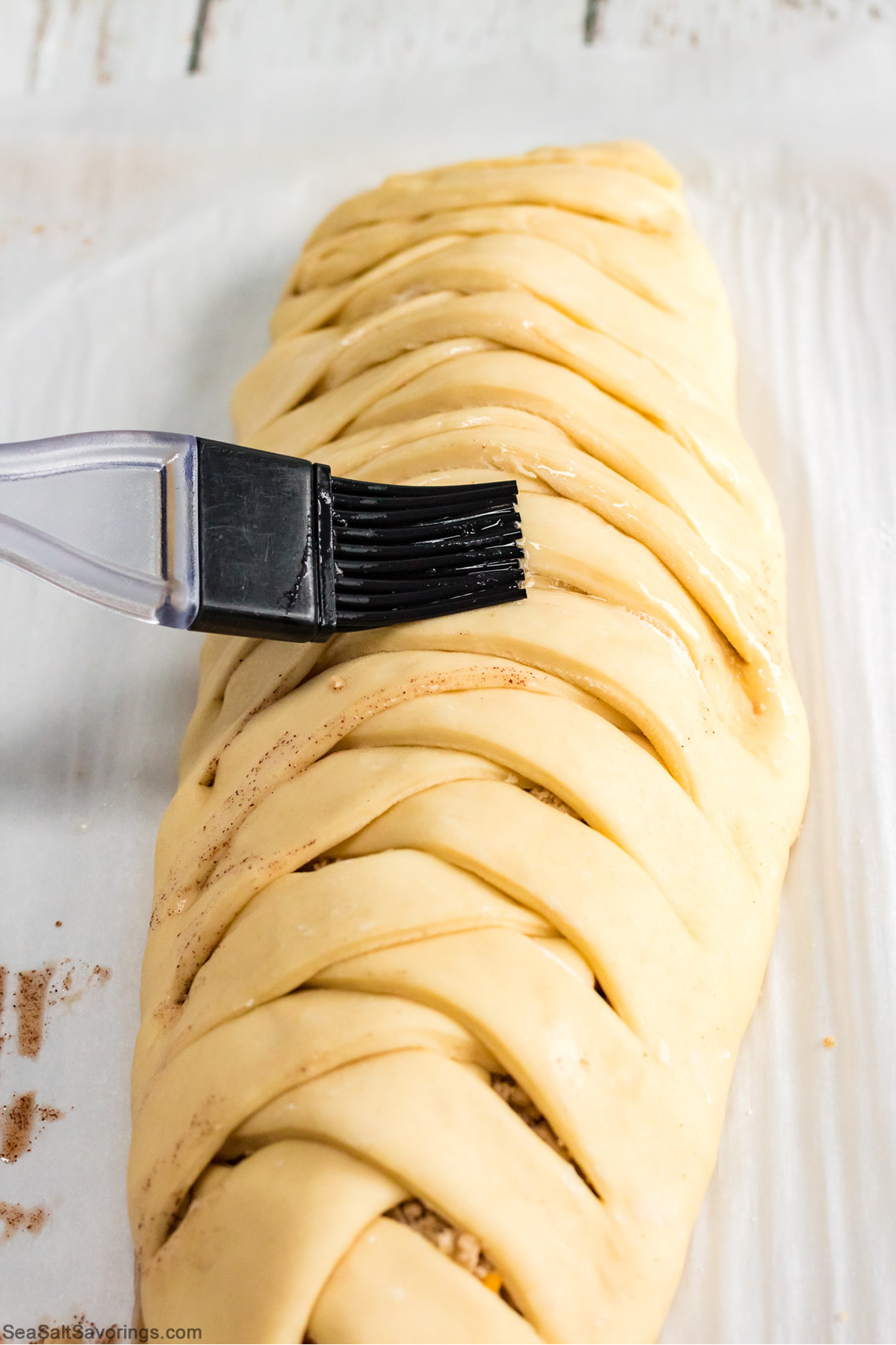 dough wrapped up into a log and getting brushed with an egg wash mixture