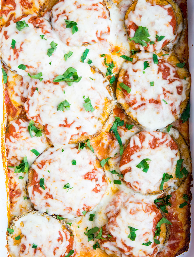 Eggplant parmesan is baked in a white baking dish and topped with parsley.