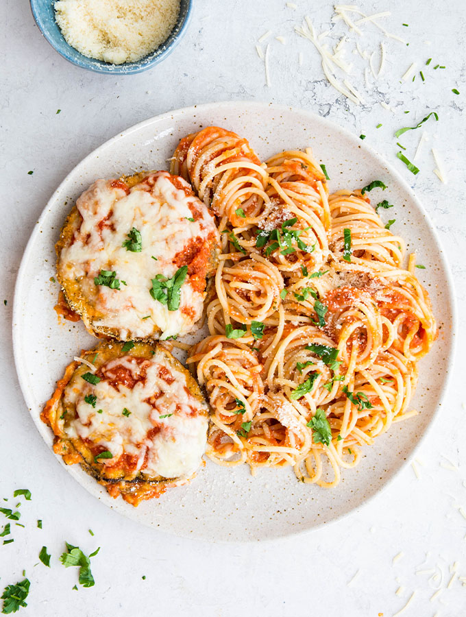 Eggplant parmesan and spaghetti is plated on a plate and topped with cheese and parsley.