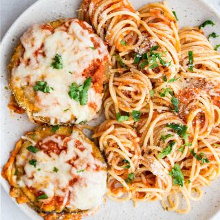 Eggplant parmesan and spaghetti pasta is plated on a speckled plate and topped with parsley.