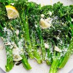 Broccolini is plated and topped with parmesan cheese and lemon wedges.
