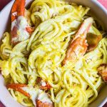 Lobster pasta is plated in a white bowl and topped with lemon zest.