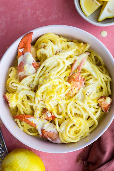 Lobster pasta is plated in a white bowl and topped with more saffron and lemon zest.